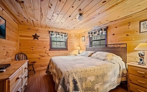 A wooden cabin bedroom with a bed, a desk, a chair, and a star decoration on the wall.