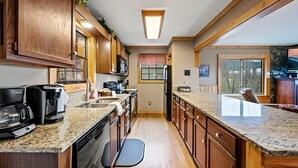 A kitchen with wooden cabinets, granite countertops, a dishwasher, and a window with a view. - Mountain Getaway with Big Views, 3 King Beds, Game Room, Hot Tub, Pet Friendly! (Sevierville)