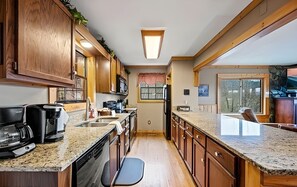 A kitchen with wooden cabinets, granite countertops, a dishwasher, and a window with a view. - Mountain Getaway with Big Views, 3 King Beds, Game Room, Hot Tub, Pet Friendly! (Sevierville)