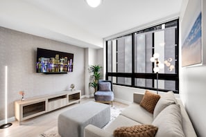 A modern living room with a flat-screen TV, a sofa, a chair, and a large window with blinds. - Luxury 1BR Downtown Miami I Free Parking + Pool (Miami)