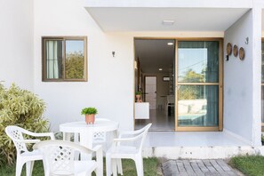 A modern building with a patio area featuring a round table and white chairs, a sliding glass door entrance, and a small potted plant. - Porto Residence (Ipojuca)