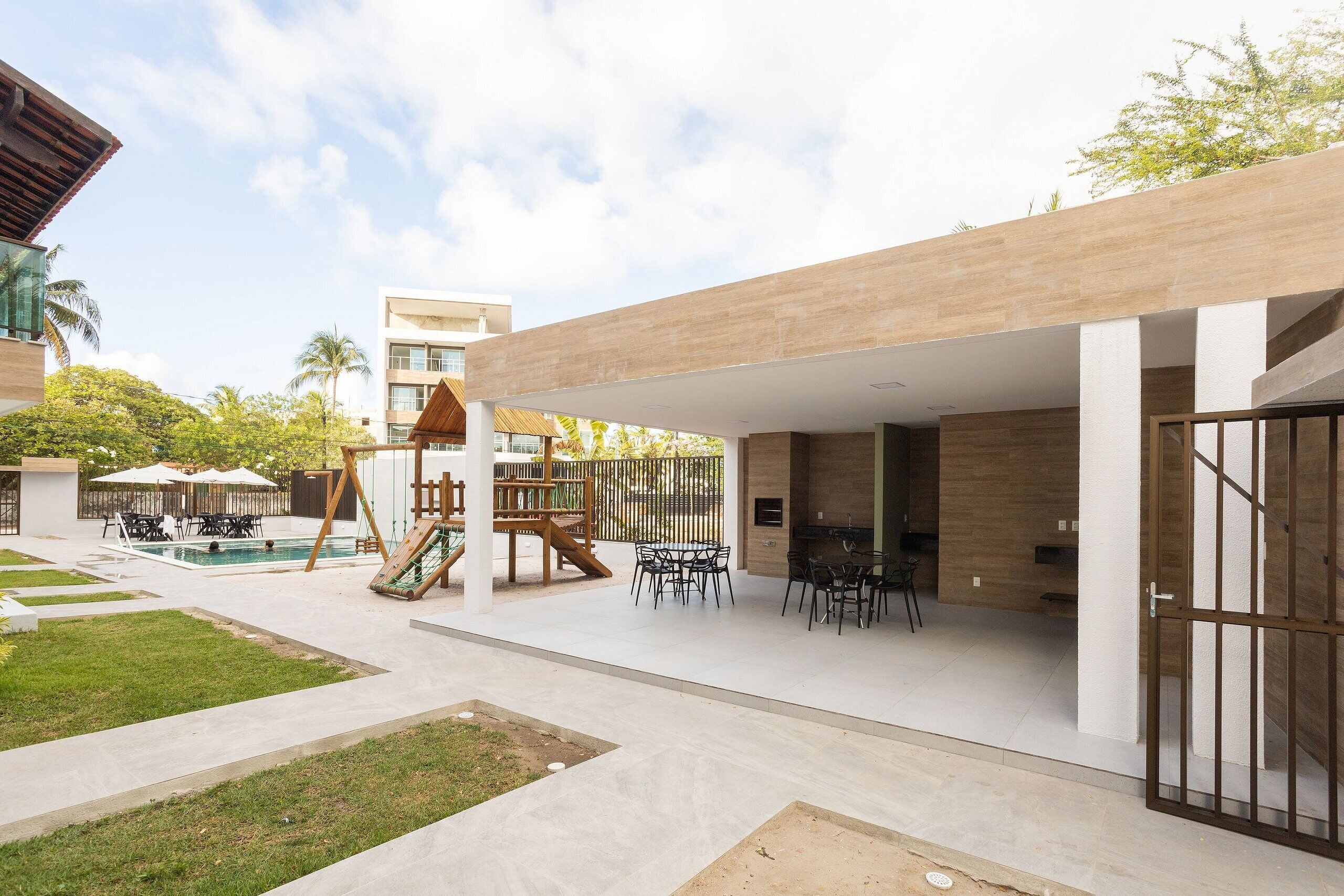 Un espacio exterior moderno con piscina, mobiliario y parque infantil.
