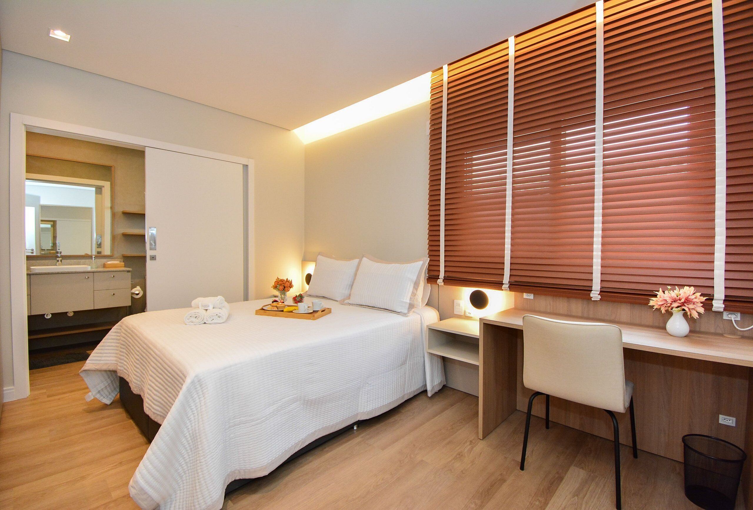 A modern bedroom with a bed, bedside table, chair, and a desk with a chair.