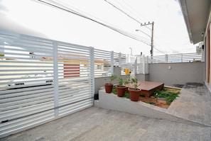 A balcony with a white metal fence, potted plants, and a wooden bench.