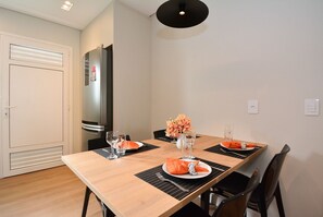 Un coin repas avec une table en bois, des sets de table noirs, des serviettes orange, des verres transparents et un vase avec des fleurs.