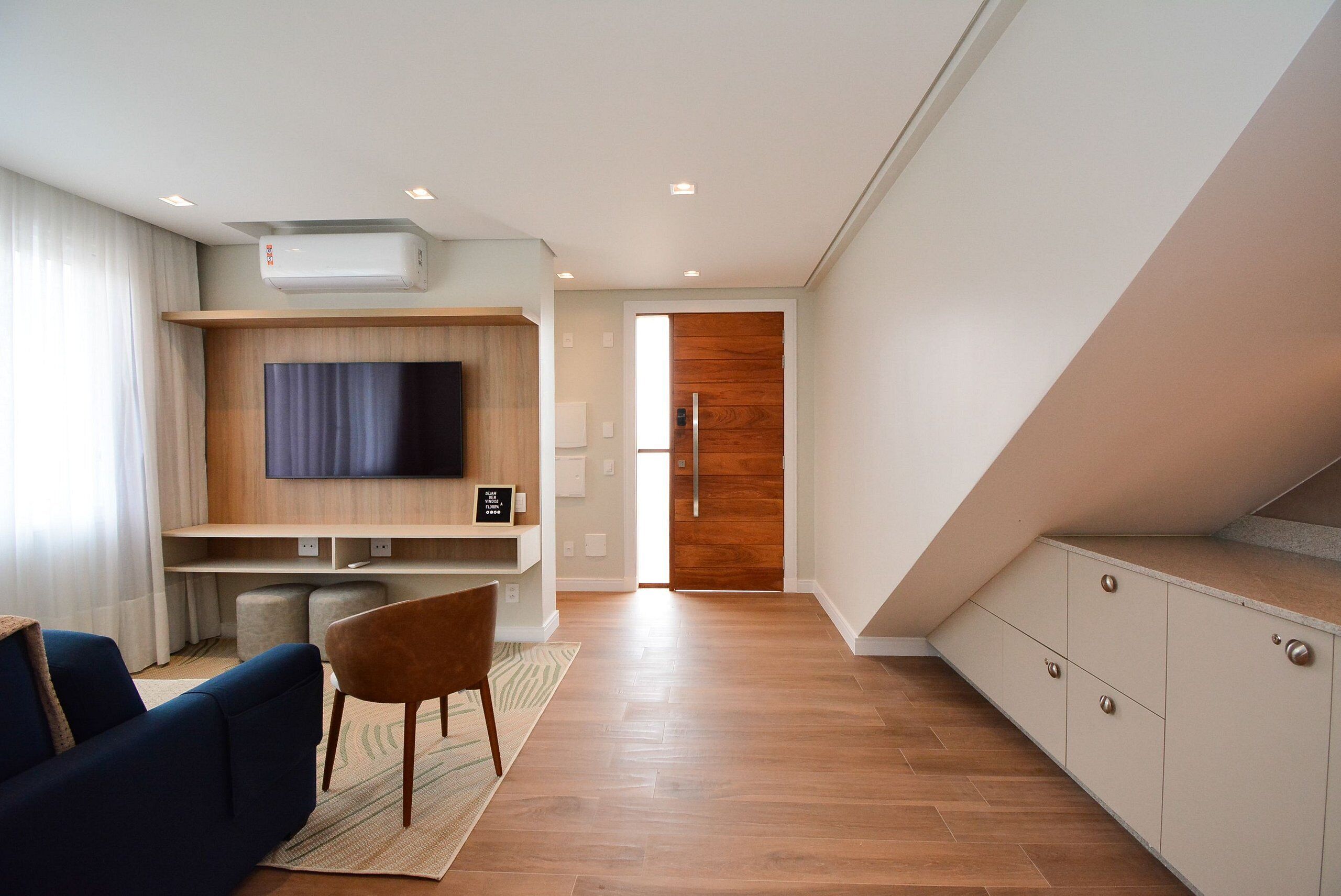A modern living room with a flat-screen TV, a sofa, a wooden cabinet, and a staircase leading to another level.