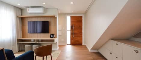 A modern living room with a flat-screen TV, a sofa, a wooden cabinet, and a staircase leading to another level.