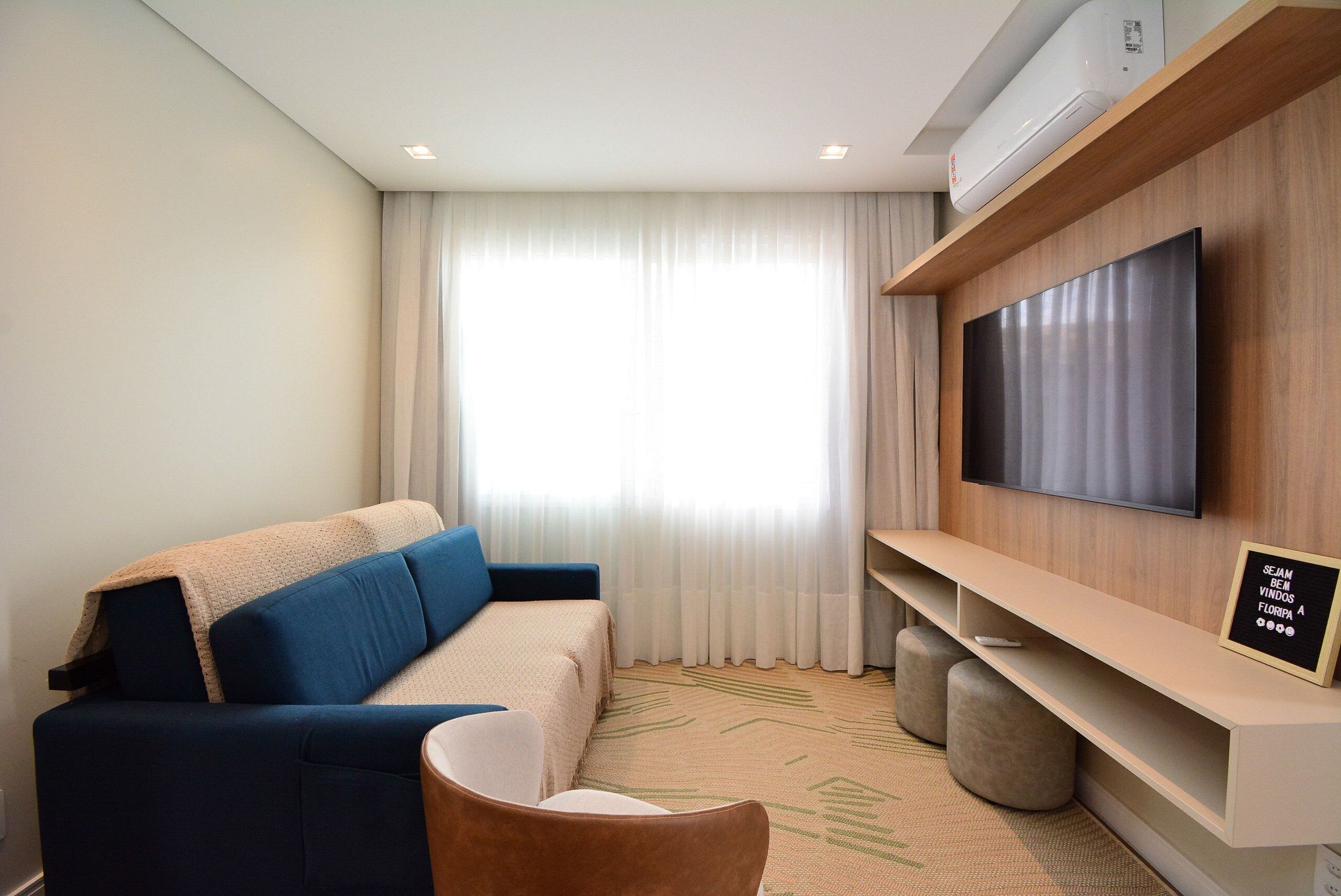 Une chambre d’hôtel moderne équipée d’un canapé, d’un téléviseur fixé au mur, d’un téléviseur à écran plat et d’un climatiseur installé au plafond.