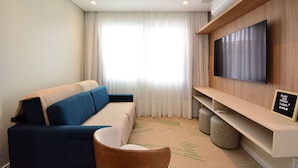 A modern hotel room with a sofa, a TV mounted on the wall, a flat-screen TV, and a ceiling-mounted air conditioner.