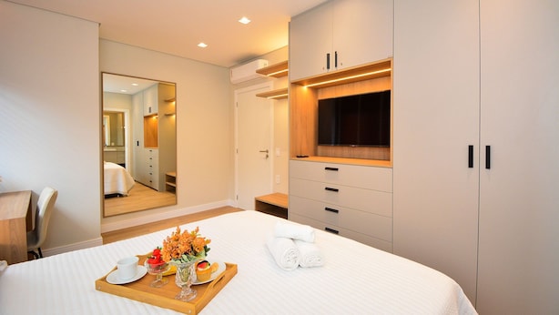 A modern hotel room with a bed, a wooden tray with breakfast items, a mirror, and a wardrobe.