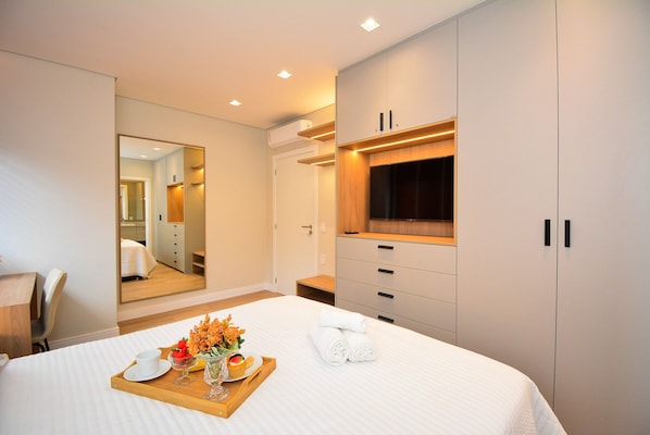 A modern hotel room with a bed, a wooden tray with breakfast items, a mirror, and a wardrobe.