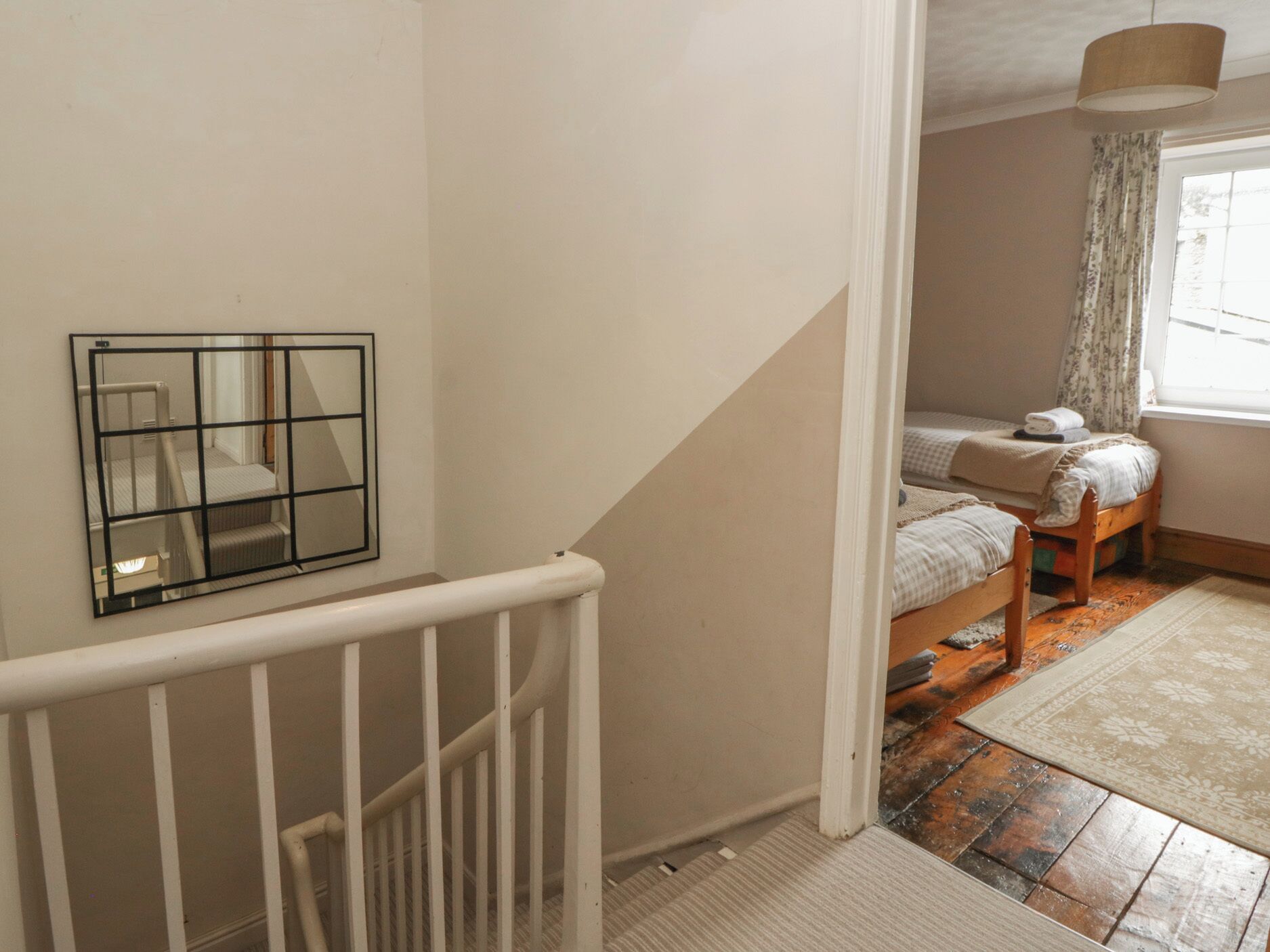 A bedroom with a bed, a window with curtains, a wooden floor, and a white railing.
