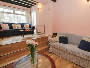 A living room with two sofas, a coffee table, a vase with flowers, and a radiator. - 1 Alpha Cottages (Tenby)