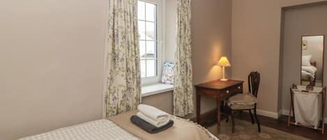 Une chambre à coucher avec un lit, un bureau avec une chaise, une lampe, une fenêtre avec des rideaux et un miroir.