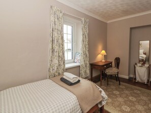 Un dormitorio con cama, escritorio y silla, lámpara, ventana con cortinas y espejo.