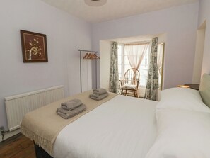 A bedroom with a bed, a chair, a radiator, a picture on the wall, and a window with curtains. - 1 Alpha Cottages (Tenby)