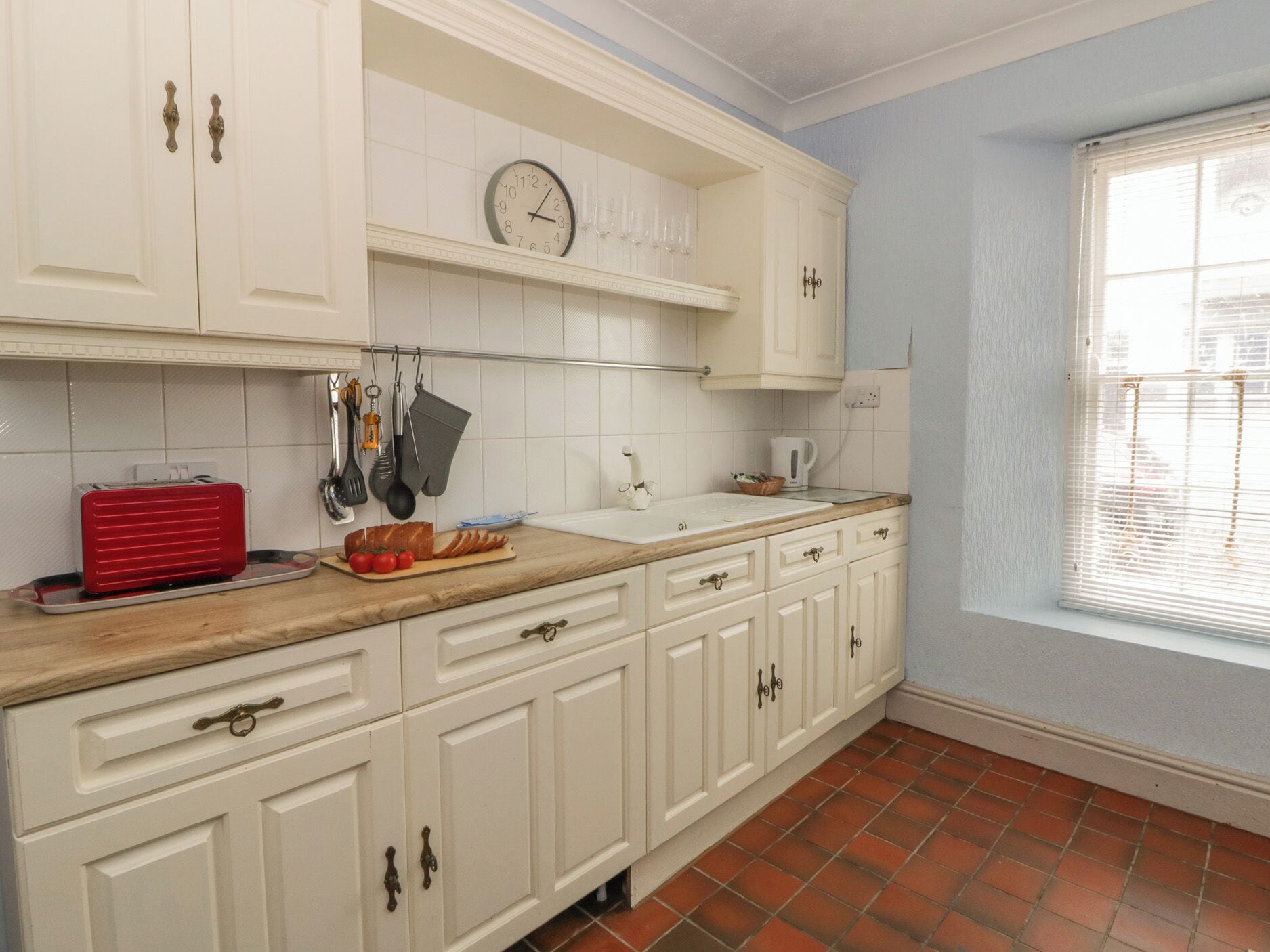 Una cocina con armarios blancos, una encimera de madera, un tostador rojo y un reloj en la pared.