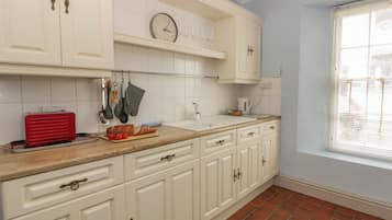 Una cocina con armarios blancos, una encimera de madera, un tostador rojo y un reloj en la pared.