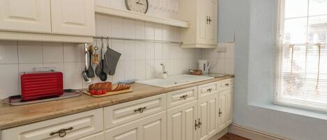 A kitchen with white cabinets, a wooden countertop, a red toaster, and a clock on the wall.