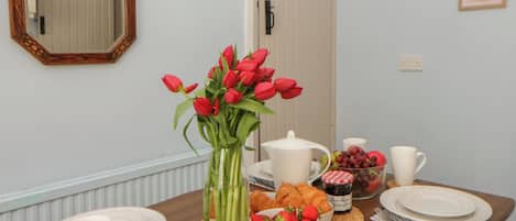 A dining table with a vase of red tulips, a teapot, a bowl of strawberries, and a plate of croissants.
