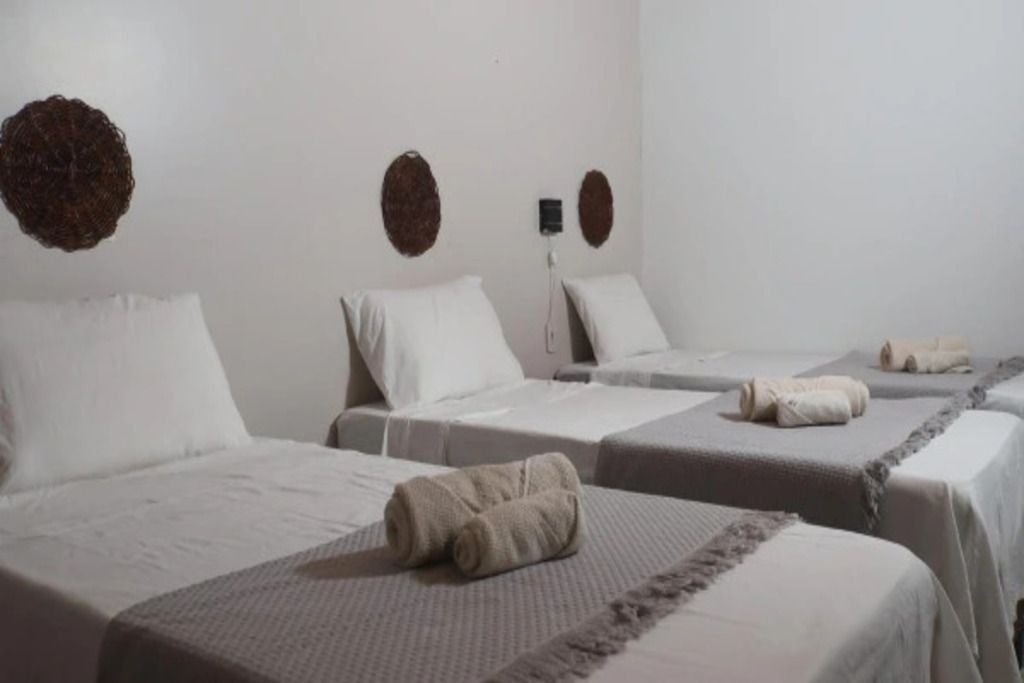A hotel room with three beds, each with a white bedspread and a rolled towel on the bed.
