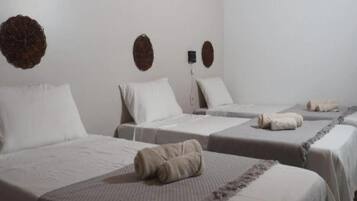 A hotel room with three beds, each with a white bedspread and a rolled towel on the bed.