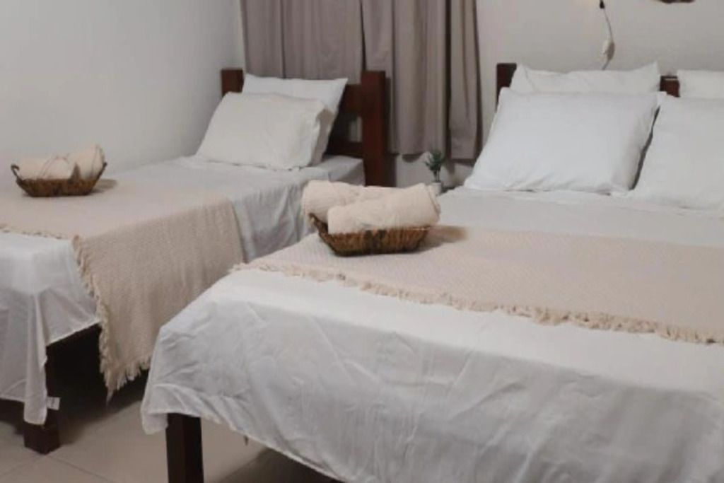 A hotel room with two single beds, each with a white bedspread and a small woven basket on the footboard.