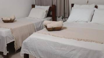 A hotel room with two single beds, each with a white bedspread and a small woven basket on the footboard.