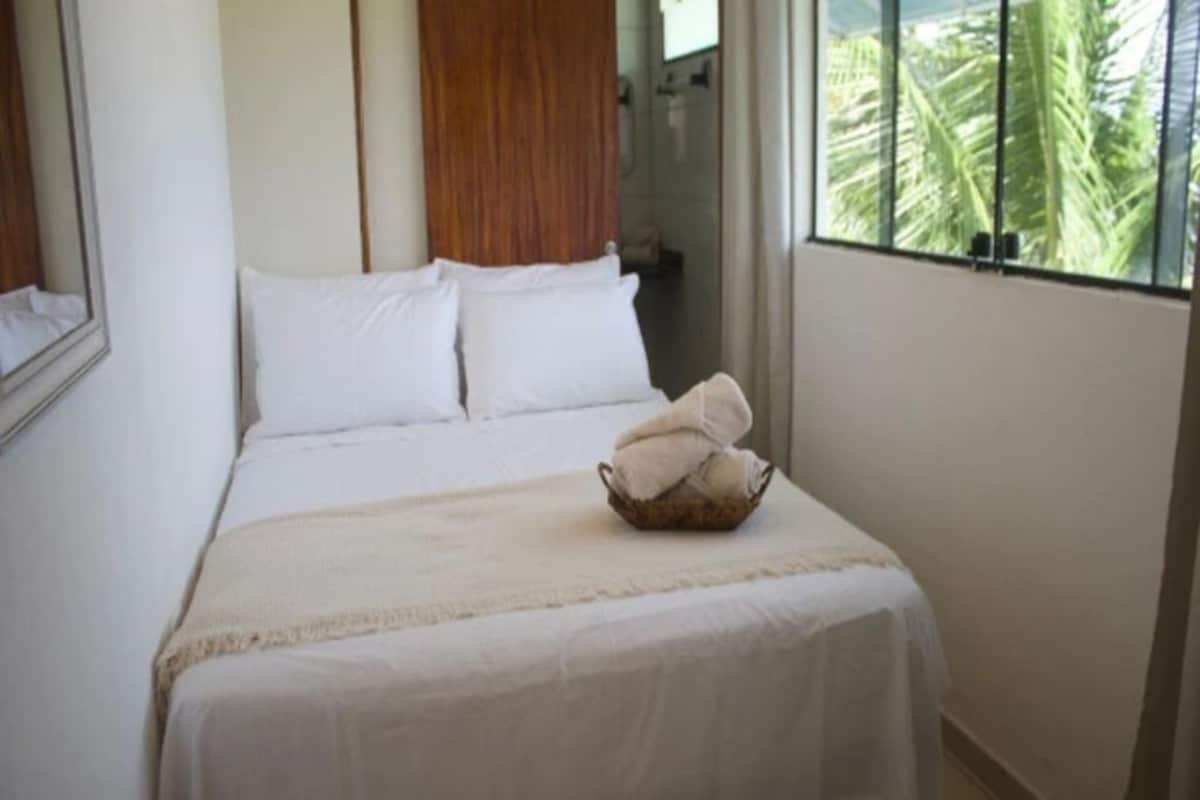 A hotel room with a bed, a window with a view of palm trees, and a wooden headboard.