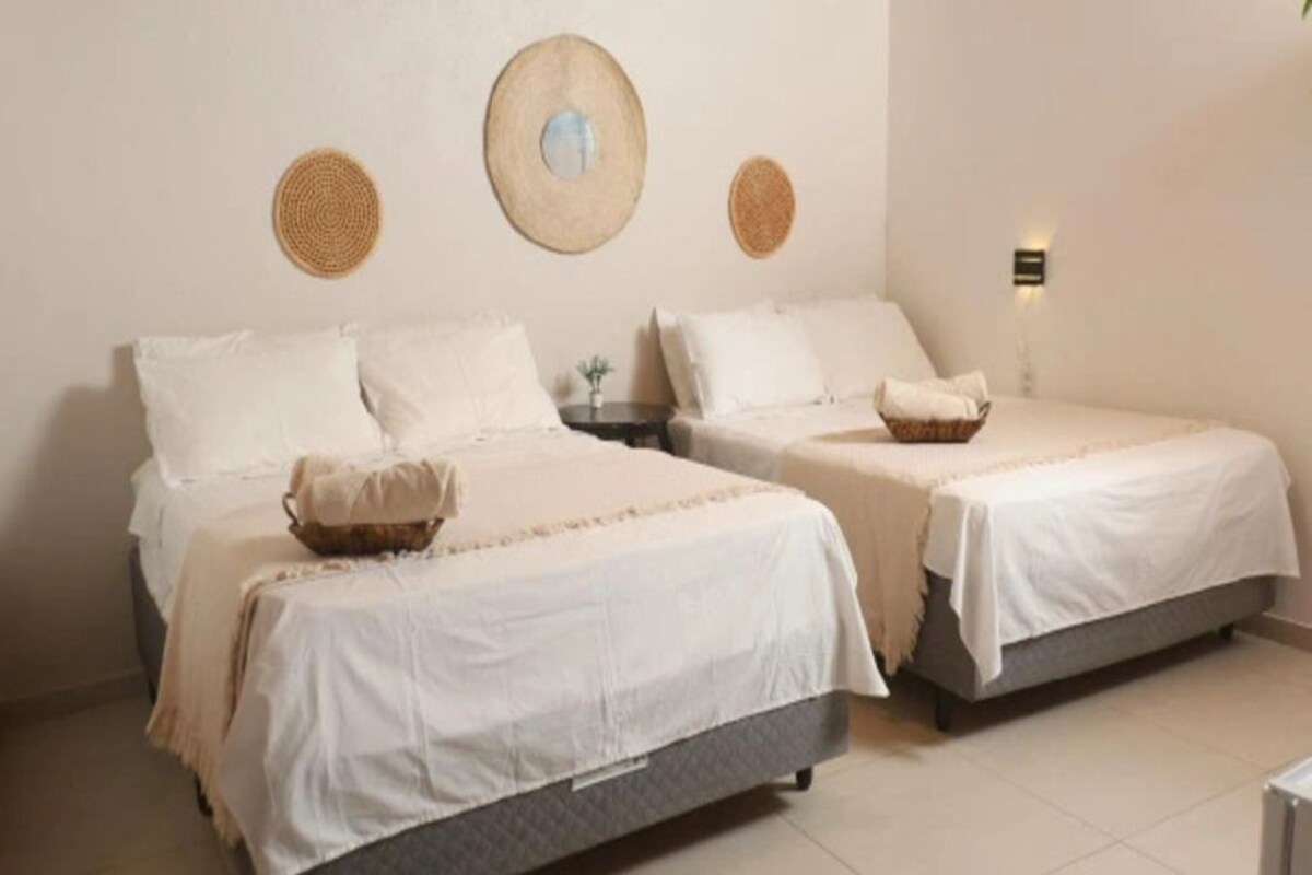 A hotel room with two beds, each with white bedding and a small woven basket on the footboard.