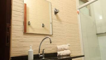 A bathroom with a black countertop, a mirror, a towel rack, and a glass shower enclosure.