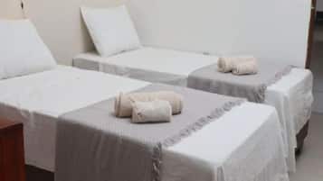 A hotel room with two single beds, each with a rolled towel and a pillow.