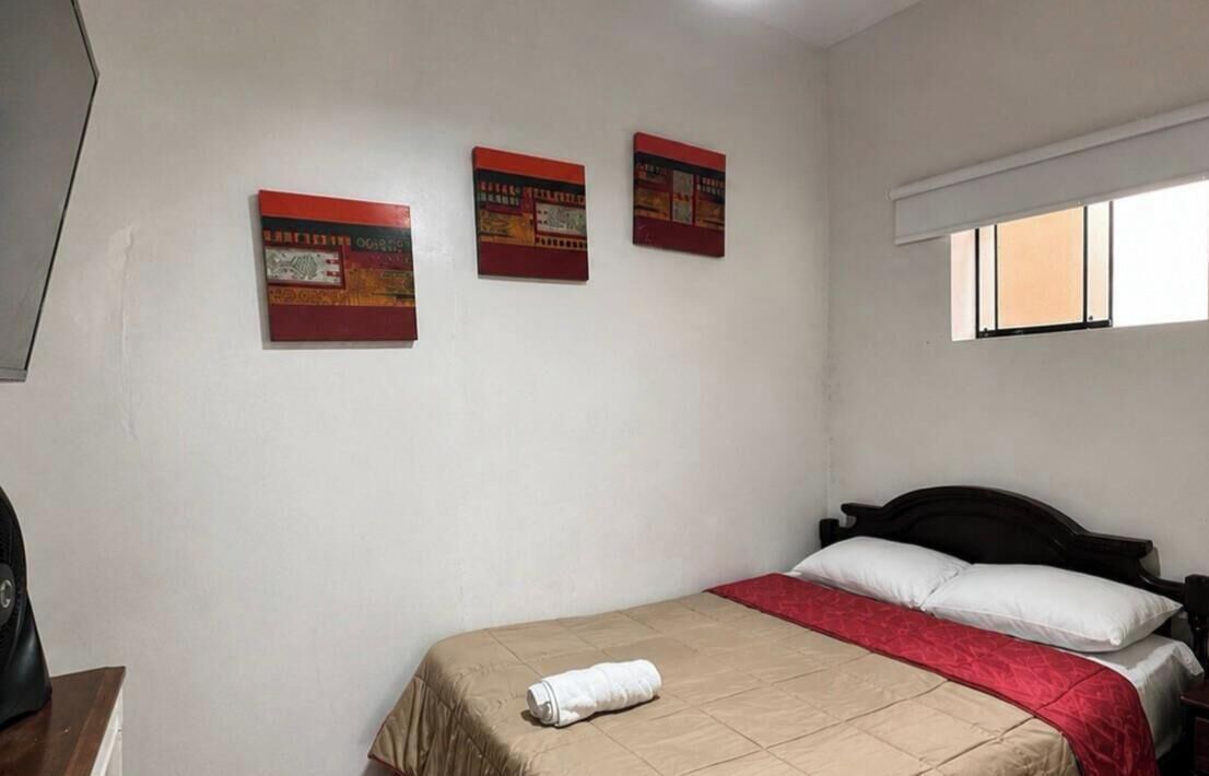 A hotel room with a bed, a window, and three wall-mounted artworks.