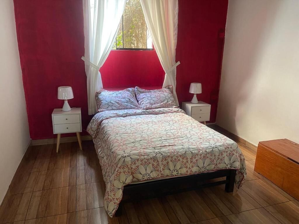 A bedroom with a bed, two bedside tables, a window with curtains, and a wooden nightstand.