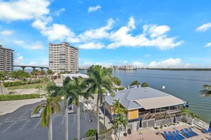 Un hôtel situé au bord de l’eau, offrant une vue sur le plan d’eau, avec un parking et un pont en arrière-plan.