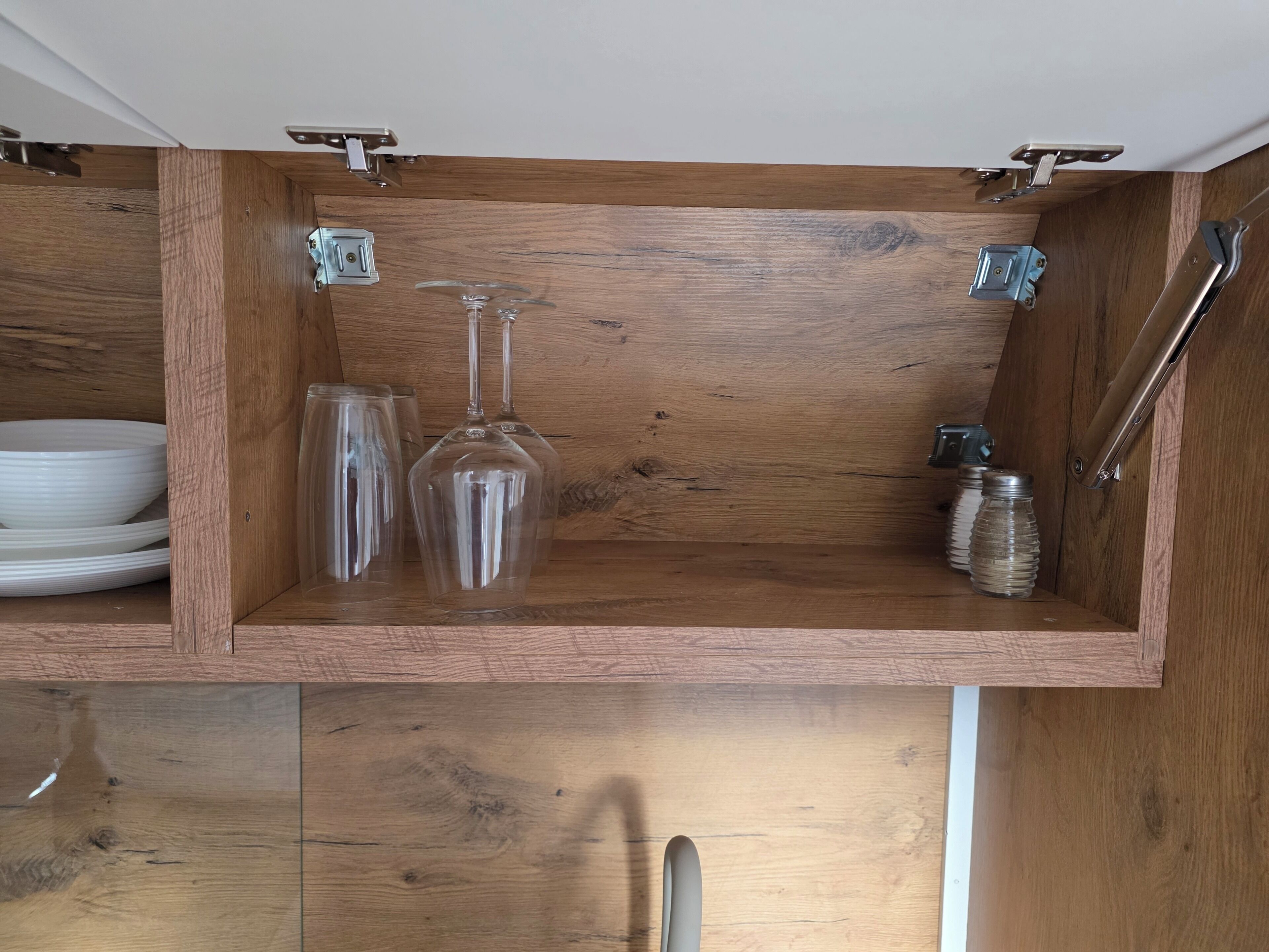 A wooden cabinet with a wine glass, a glass, and a metal container.