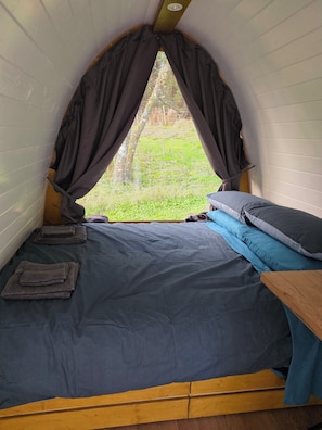 Una habitación pequeña y acogedora con cama, una mesa de madera y una ventana con cortinas.