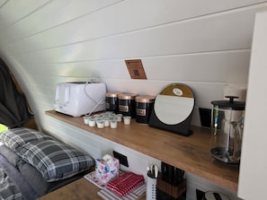 A kitchenette with a toaster, coffee maker, sugar and cream containers, a mirror, and a knife block.
