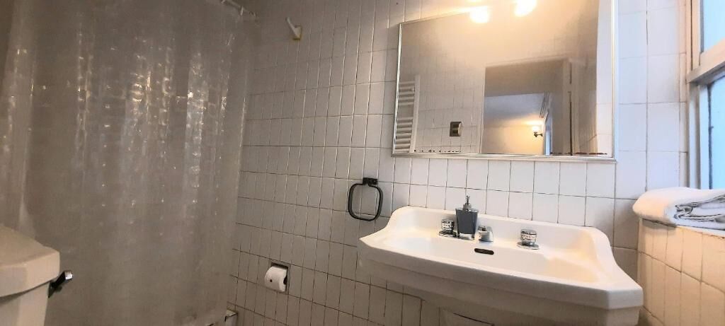A bathroom with white tiles, a sink, a mirror, and a towel rack.