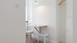 Ein Zimmer mit Holzboden, weißen Wänden, einem Schreibtisch mit Pendelleuchte und einem Kleiderständer.