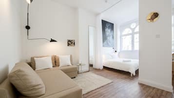 A modern bedroom with a bed, a sofa, a small table, and a wall-mounted lamp.
