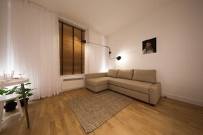 A living room with a beige sectional sofa, a wooden floor, a patterned rug, a dining table with chairs, a potted plant, and a wall-mounted picture. - The Holborn Hideaway by The Design Traveller (London)