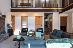 A spacious living area with a high ceiling, a fireplace, a sofa set, and a dining table. - The Avondale Lake House (Hayden)