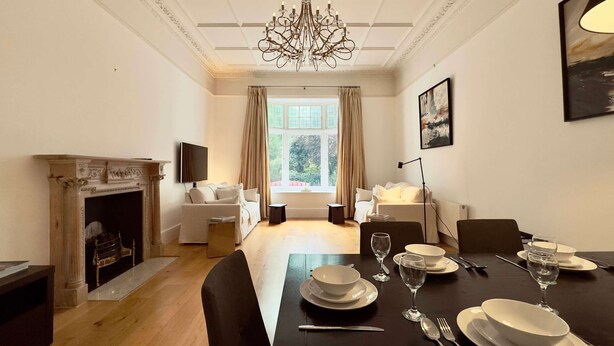 Ein Esszimmer mit Kamin, einer Chandelierleuchtre und einem für vier Personen gedeckten Tisch.