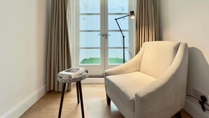Ein Zimmer mit einem weißen Sessel, einem kleinen Tisch mit einer Zeitschrift, einer Stehlampe und einer Tür mit Glasfenstern.