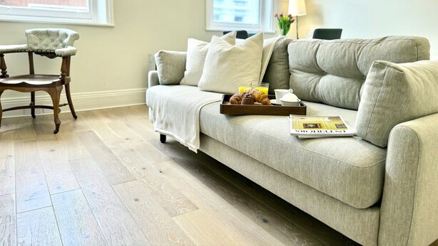 A living room with a sofa, a wooden chair, a tray with croissants and a book, and a window with a view of buildings. - Chic Marylebone Village  Premium Mattress   55   TV (London)