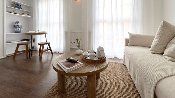 A living room with a sofa, a coffee table with books and a remote, a small table with a vase and cups, and a bookshelf. - Chic Marble Arch w  100  Cinema   Premium Mattress (London)