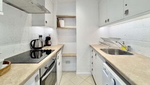 A compact kitchen with a stove, oven, sink, and dishwasher. - Chic Marble Arch w  100  Cinema   Premium Mattress (London)