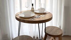 A round wooden table with two stools, set against a window with sheer white curtains. - Chic Marble Arch w  100  Cinema   Premium Mattress (London)