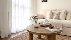 A living room with a round wooden coffee table, a beige sofa, and a white vase with flowers. - Chic Marble Arch w  100  Cinema   Premium Mattress (London)